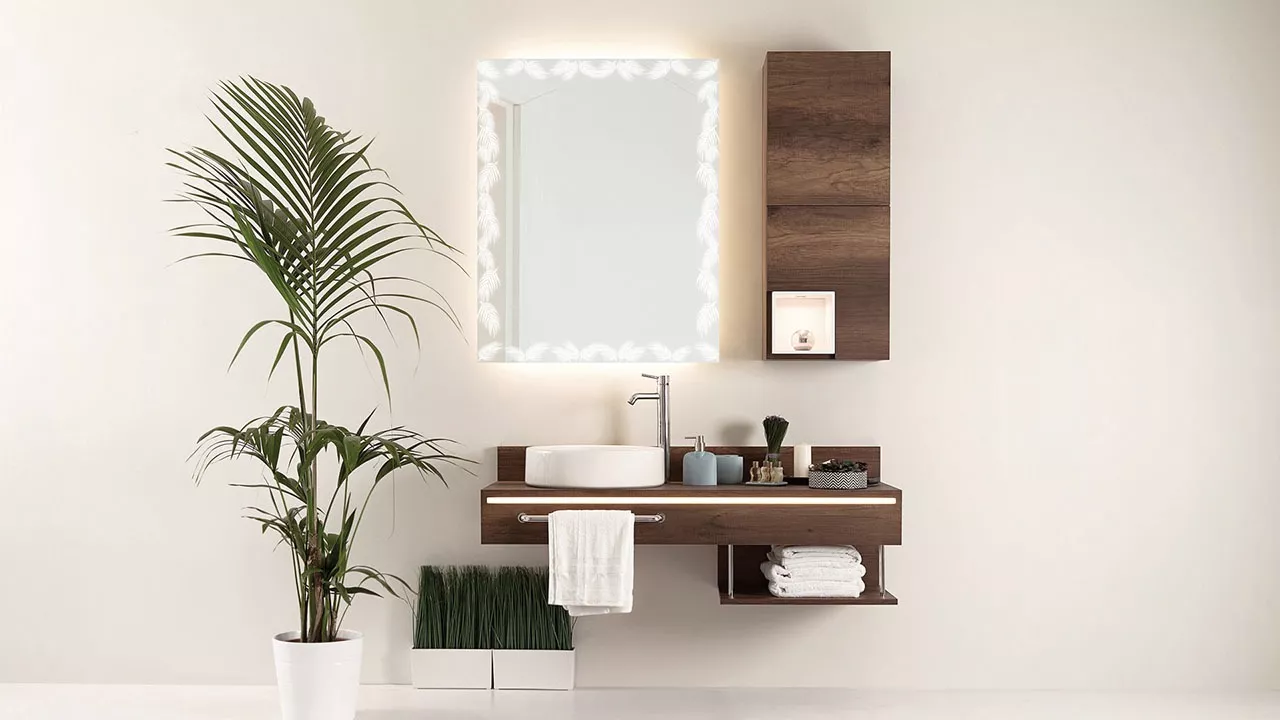 Lighted mirror with nature frame design on a clean wall above a wooden cabinet and a sink in Kuwait.